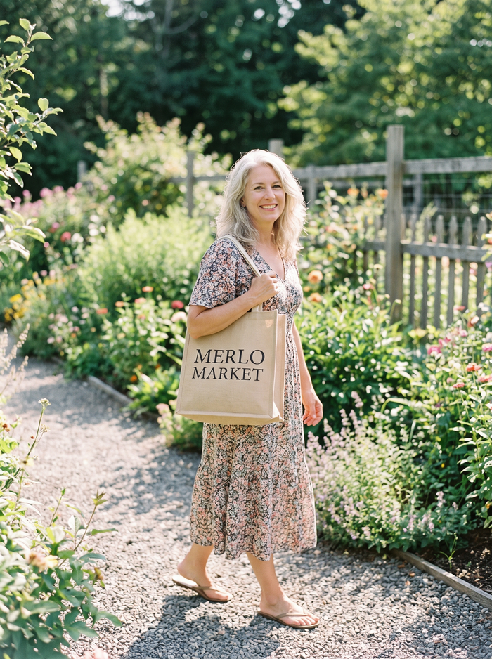 Woman in a dress walking through a garden with a Merlo Market tote